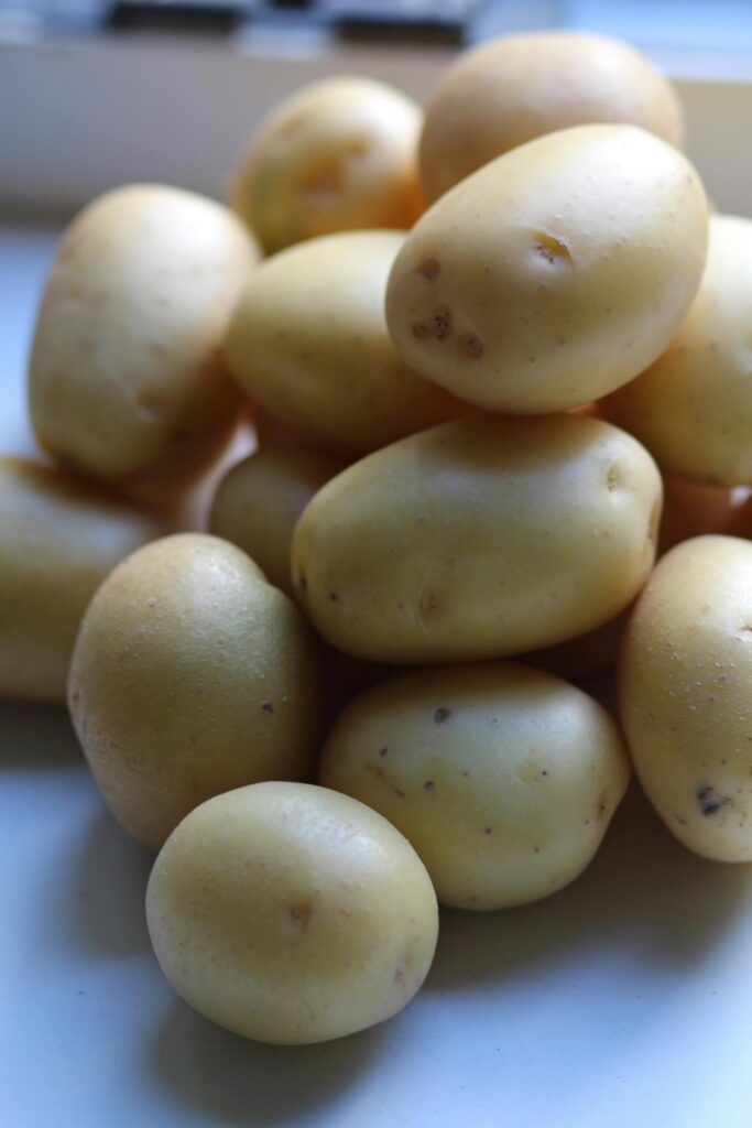 A close-up image showcasing fresh yellow potatoes piled on a ceramic plate.